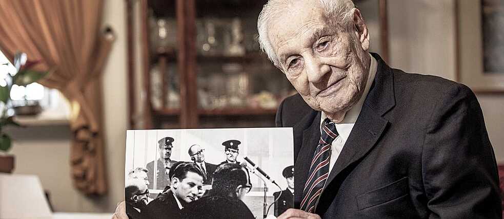 גבריאל בך, 94, בביתו בירושלים. בתמונה ההיסטורית ניתן לראותו במרכז, כשמאחוריו אדולף אייכמן על ספסל הנאשמים בתא הזכוכית.