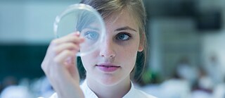 Ein Mädchen hält eine Petrischale vor ihrem Auge