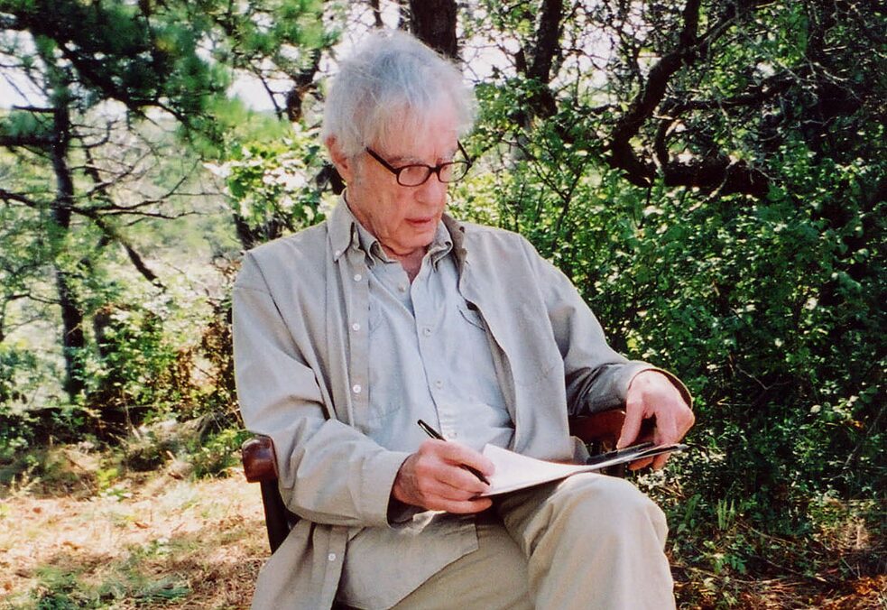Der Psychologe Robert Jay Lifton in hohem Alter sitzt draußen in der Natur auf einem Stuhl und blickt auf ein Papier auf seinem Schoß. 