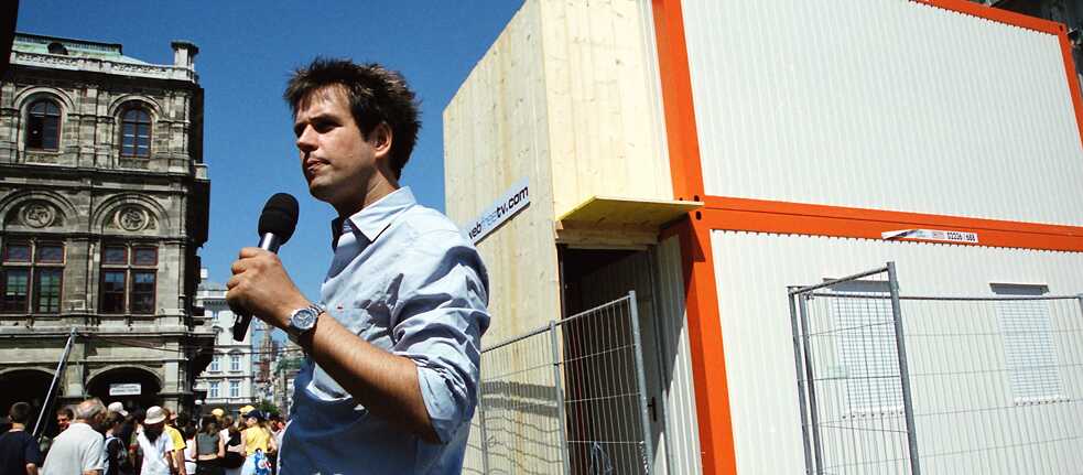 Christoph Schlingensief in front of his container during the 2000 Vienna Festival: Based on the “Big Brother” concept, twelve participants presented as “asylum seekers” lived here – eight cameras broadcast their lives live on the internet so that the audience could select two applicants for deportation every day.