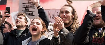 Bild aus dem Film Und morgen die ganze Welt: Vier junge Leute stehen lachend und klatschend auf einer Demonstration.