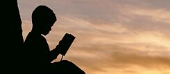 Et barn leser en bok utendørs foran en solnedgang