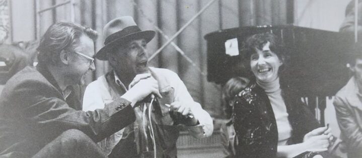 A black&white photo. From left to right Rudolf Bahro, Joseph Beuys and Rhea Thönges-Stringaris are seated on a stage. In the background you can see the rear part of a grand piano.