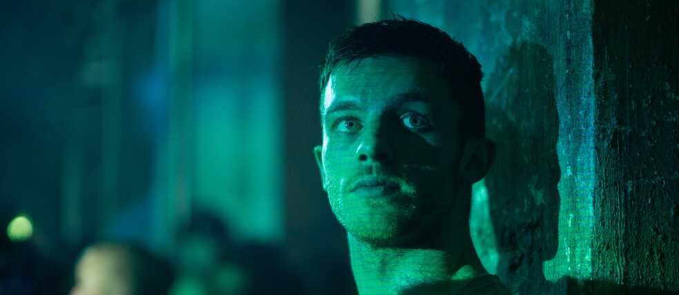 Standbild aus der Amazon Prime Serie “Beat”: der Club Promoter Beat ( Jannis Niewöhner) lehnt in grünem Licht gebadet an einer Beton Säule