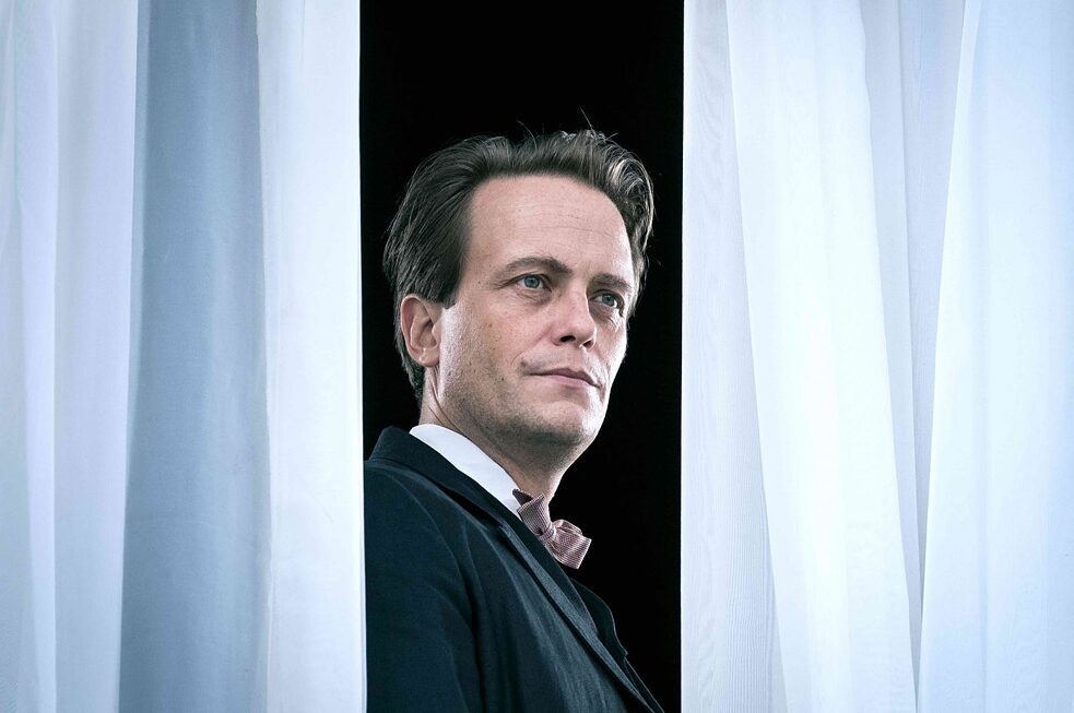 Stillframe from the series “Bauhaus - A new Era": August Diehl as Walter Gropius looking between two curtains