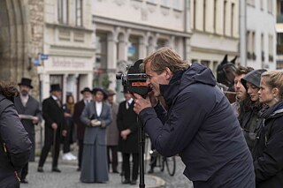 Behind the scenes of the series “Bauhaus - A new Era": Director Lars Kraume on the set, looking through a camera during the shoot. 
