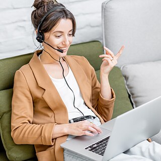 Eine lächelnde junge Frau mit Headset lernt am Laptop.