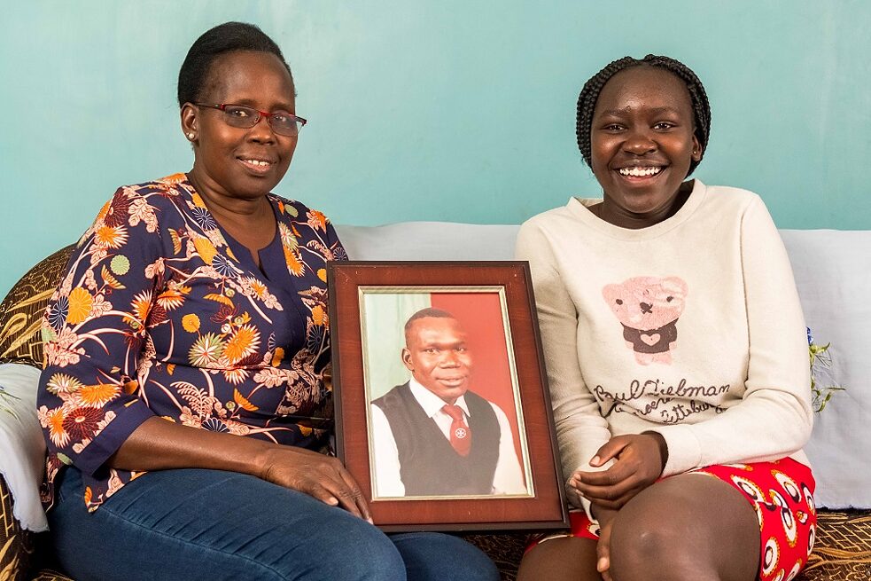 Lucy with one of her five refugee children. They hold a portrait of the deceased husband