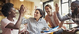 Junge Leute lachen und klatschen sich ab. Sie halten Schnellhefter, Tablets und Handys in der Hand.