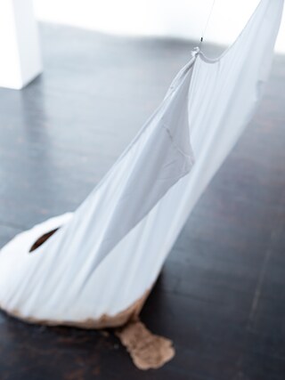 No Brasil, as estatísticas sobre violência contra a mulher, feminicídio e genocídio das populações negras e indígenas são ultrajantes. Minhas reflexões sobre a violência contra corpos e terras levaram à escultura “Barragem”: um lençol cheio de lama que transborda por uma fenda. O corpo é sugerido pelo lençol, e pelo corte flui uma matéria tóxica que não pode mais ser ignorada. “Barragem” – lençol e terra; 80 x 80 x 160 cm; 2019. 