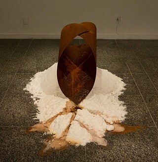 Após o impacto catastrófico do colapso das barragens de minério de ferro em Mariana e Brumadinho, em Minas Gerais, comecei a pensar na atividade de mineração como uma hemorragia.  O ferro da Terra e o ferro do sangue. “Minério-Hemorragia” é uma escultura arredondada em ferro colocada sobre uma pilha de sal por onde escorre uma hidrografia de ferrugem e terra coletada em áreas próximas à mineração. “Minério-Hemorragia” – ferro, sal, ferrugem e terra; 150 x 80 x 80 cm; 2018.