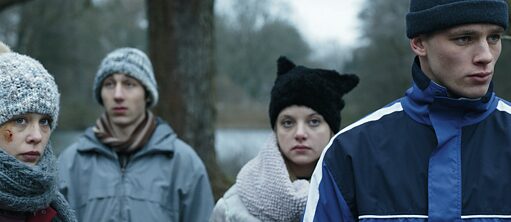 Vier Jugendliche in Winterkleidung stehen versetzt nebeneinander. Ihre Blicke sind ernst und in die Ferne gerichtet. 