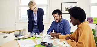 Zwei Schüler*innen mit einer Lehrerin in einem Klassenzimmer