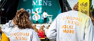 To unge i trøjer med "Ungdommens Folkemøde"-logoer står foran en scene.