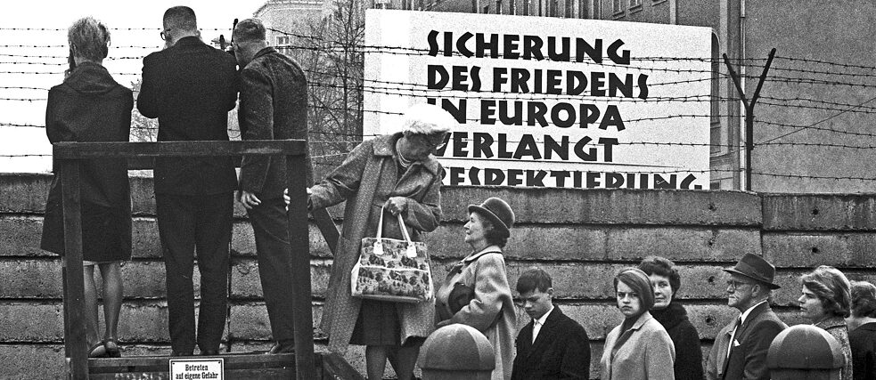 Berlin, 1962. Menschen stehen auf einer Leiter auf der Westseite der Berliner Mauer, um einen Blick auf die andere Seite der Grenze zu werfen.
