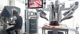 Operační robot da Vinci: Vlevo operuje člověk ve virtuálním prostoru, vpravo operují robotická ramena s dálkově ovládanými nástroji – zde při testování na modelu.