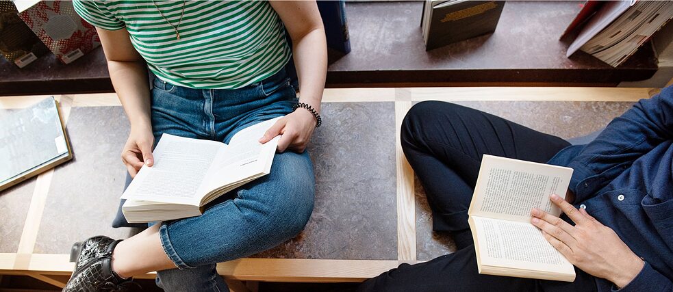 Zwei Personen sitzen auf einer Bank und lesen Bücher.