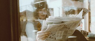 Eine Frau liest in einem Café Zeitung. 