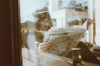 Eine Frau liest in einem Café Zeitung. 