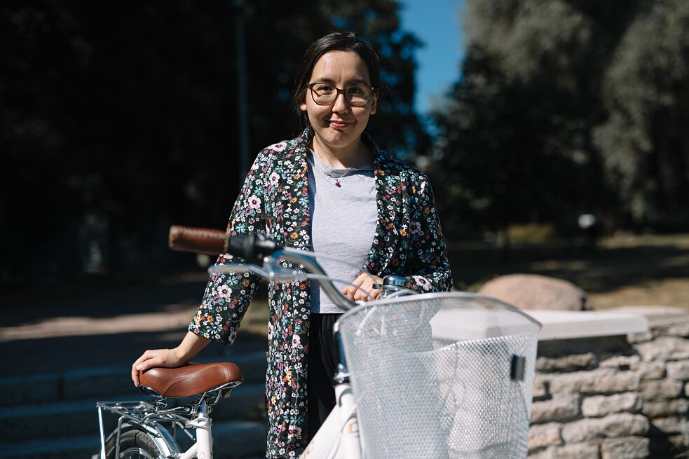 Tumedapäine noor naine seisab valge jalgrattaga