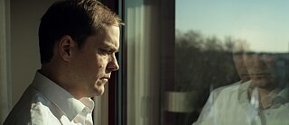 Un hombre parado frente a una ventana se refleja en ella