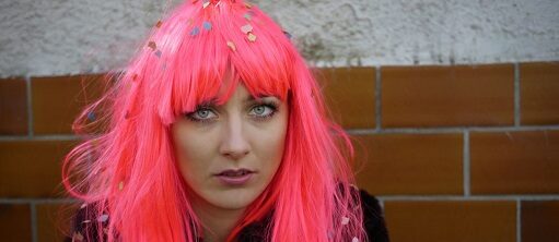 Junge Frau mit langen pinkfarbenen Haaren vor Bachsteinwand