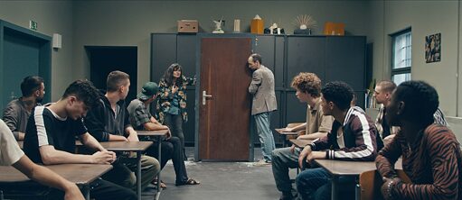 Fox in a Hole - film still: two teachers hold a door frame, the students look at them