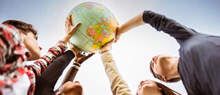 Several young people hold up a globe together