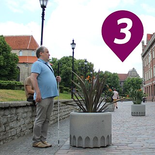 Artur Räpp, Vorstandsmitglied des Blindenverein Nord-Estland, steht vor einem großen Blumenkübel, welcher eine Straßensperre darstellt.