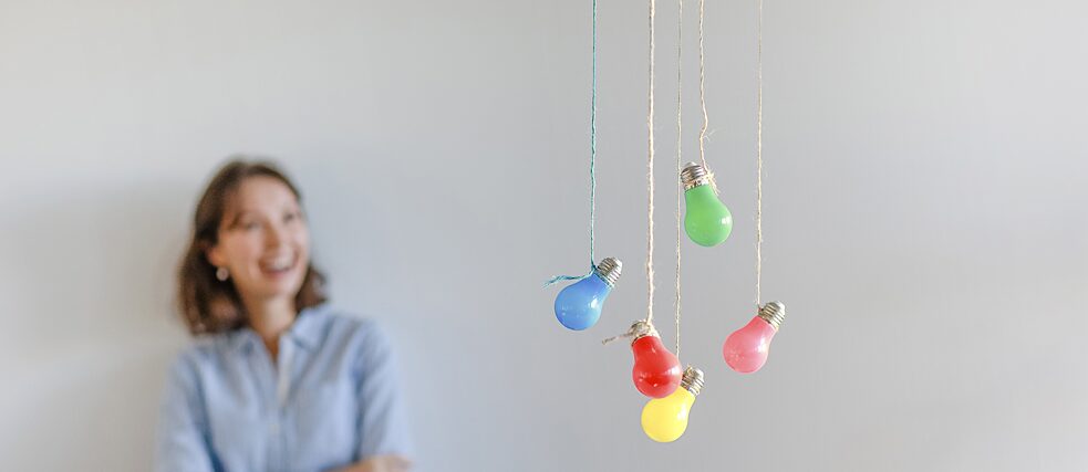 Colourful light bulbs dangle from the ceiling. A young woman stands in the blurred background.  