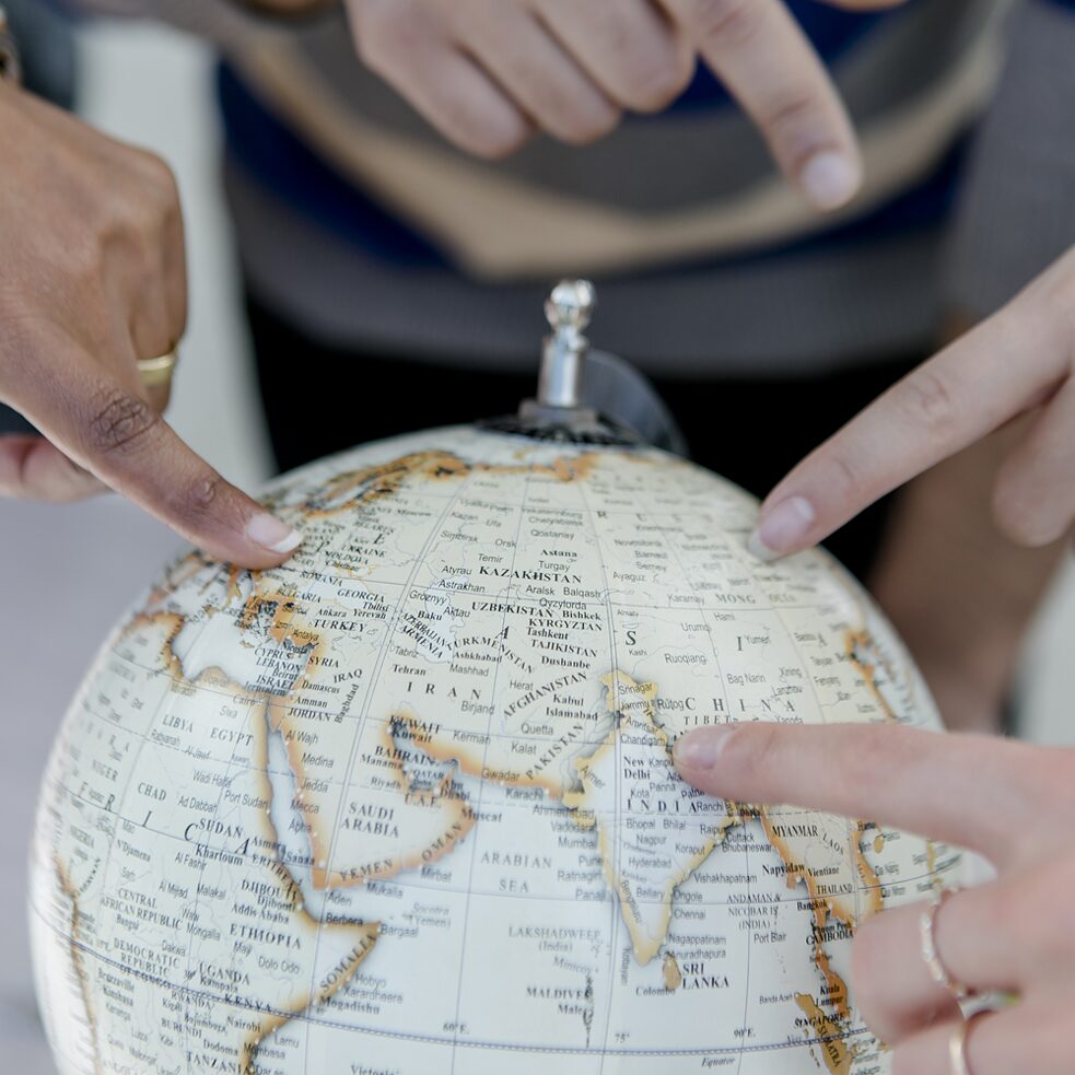Vier Hände mit verschiedenen Hautfarben zeigen auf einen Globus