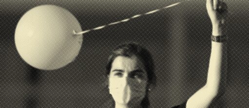 Kumral bir kadın sol kolunu kaldırmış ve beyaz bir balonu kurdelesinden tutuyor. Siyah bir tişört ve beyaz bir ağız-burun maskesi takıyor.