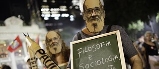 Latitude – Menschen tragen Masken von Paulo Freire während eines Protests in Rio de Janeiro, Brasilien.