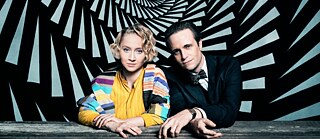 Key art from the series “Bauhaus - A New Era“: Anna Maria Mühe as Dörte Helm and August Diehl as Walter Gropius in front of a abstract spiral vortex painting.