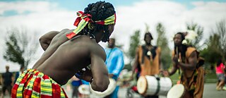 Latitude – An African man dancing in front of musicians with drums in a park