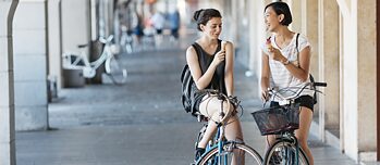 Two women on a bicycle eating ice cream