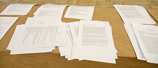 The picture shows stacks of paper sheets next to each other with texts printed on them.