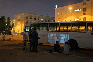 موقف سيارات خال في منطقة محيصنة يتحول إلى سينما/ مسرح مؤقت عندما يعرض مجموعة من الأصدقاء فيديوهات موسيقية باستخدام البروجكتور على جانب حافلة متوقفة.