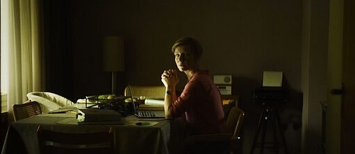 Escena del film "Exilio" con mujer sentada a una mesa en una habitación en penumbras