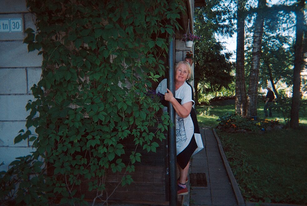 Sommerhaus im Wald, die Frau schaut hinter einer Rebe hervor, die vom Dach des Hauses herabsteigt