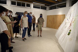 The photo shows a group of people standing in a semicircle around the curtain, one of the artworks. You can see some materials that were attached to the curtain.