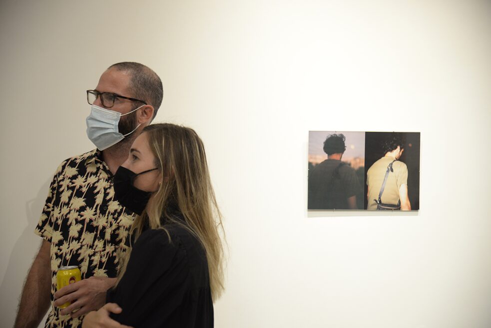 On the left side of the image you can see a man and a woman looking at something. In the right side of the image, you can see a photograph showing two people from behind.