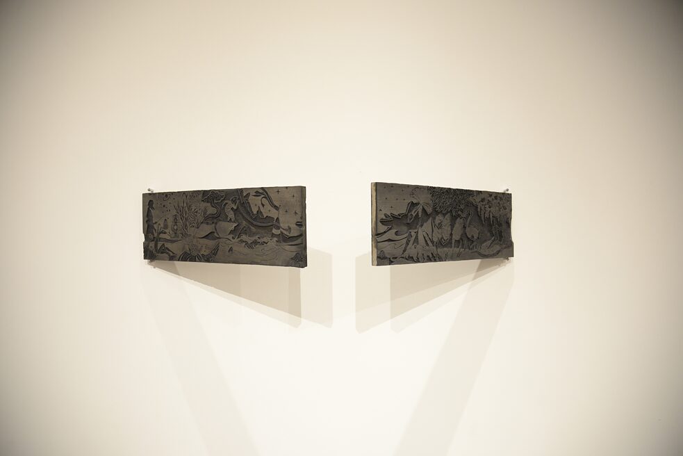 Das Bild zeigt zwei aus Holz geschnitzte Werke. Die Werke sind vor einer Wand befestigt und zeigen zwei unterschiedliche Naturmotive.