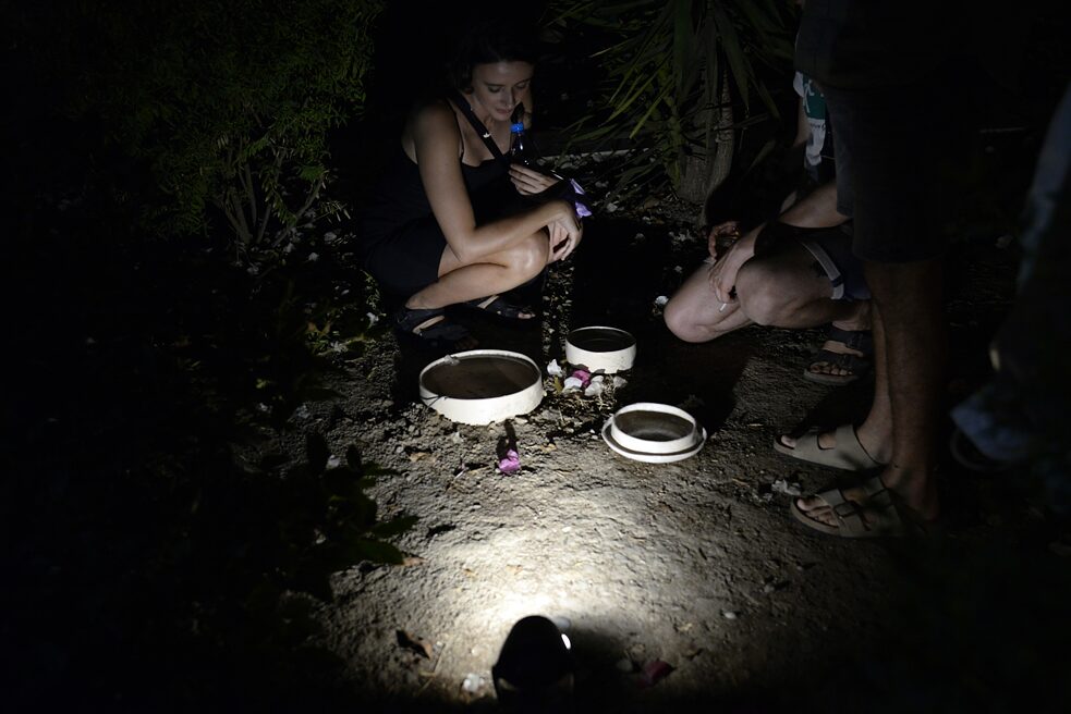 In the picture you can see three ceramic bowls, which are illuminated in the dark. Behind them kneels a woman. Two more people are standing to the side of it.