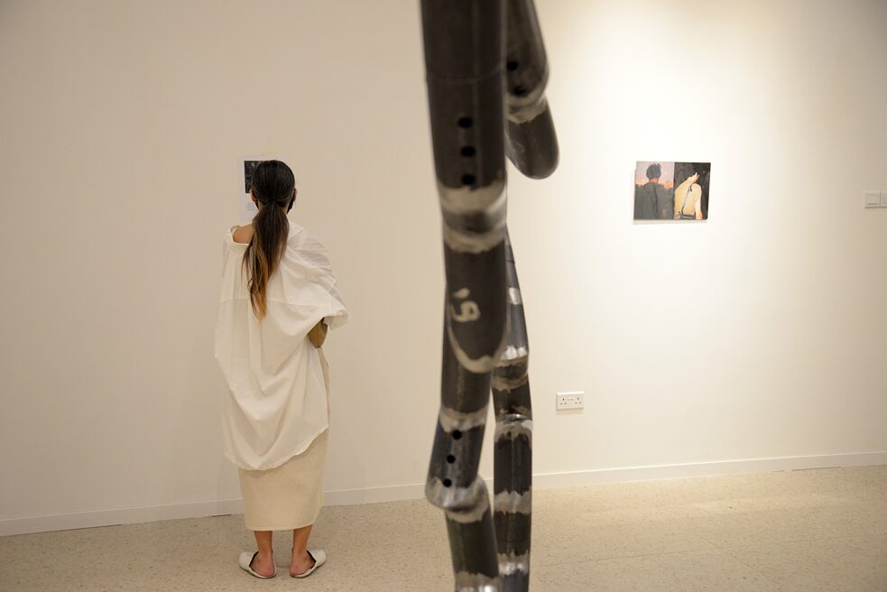 A woman is reading the description to one of the artworks. Next to her is another work. It is one of the photographs.
