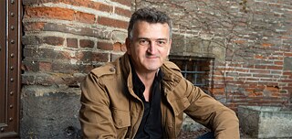 Mann sitzt vor Gebäudemauer