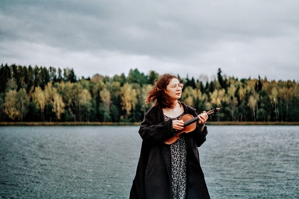 Eine junge Frau in der Natur, in der Hand eine volkstümliche Geige. 