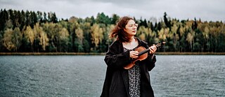 Eine junge Frau in der Natur, in der Hand eine volkstümliche Geige. 