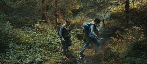 Zwei Jungen wandern durch einen Wald. Sie tragen jeweils einen Rucksack.