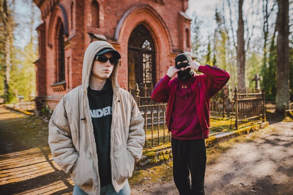 Zwei junge Musiker stehen am Tor eines Friedhofs. 